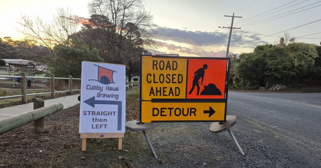 Road closed and detour sign next to our sign saying to go straight then left