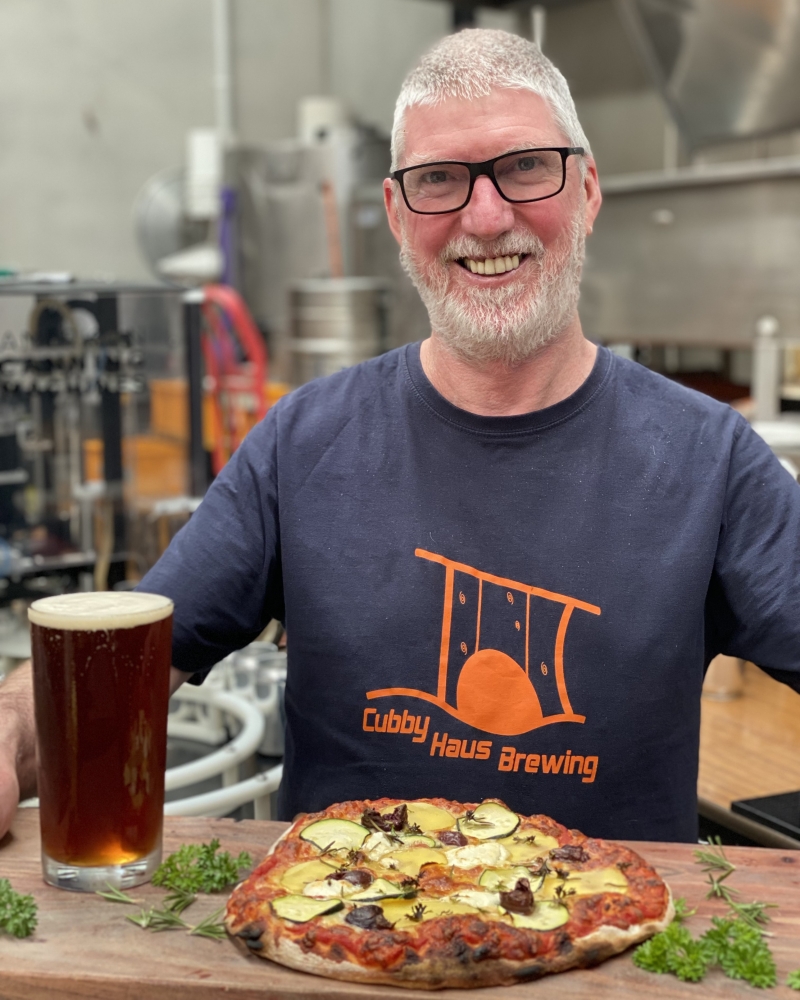 Malcolm holding a wooden plater with a pint of beer and a pizza