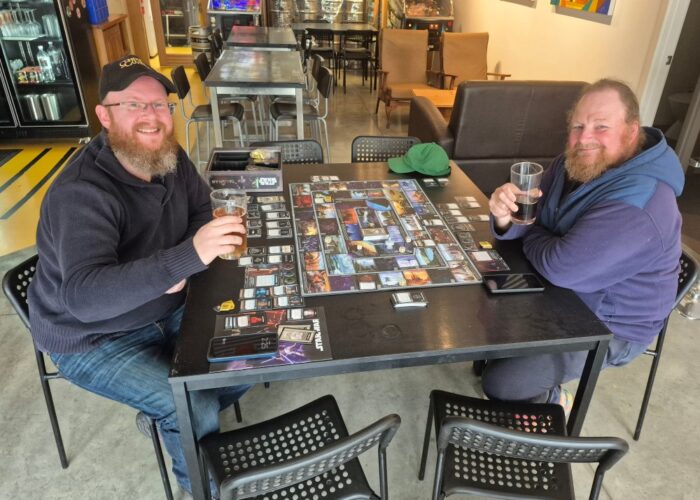 Two gents playing a complex board game enjoying a beer